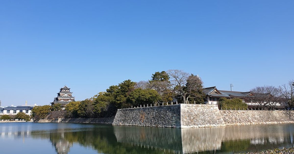 Scenic view of Hiroshima Castle with reflection in moat under a clear blue sky.
