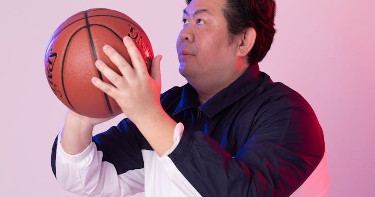 Man in sports clothing posing with a basketball, looking up in a studio setting.