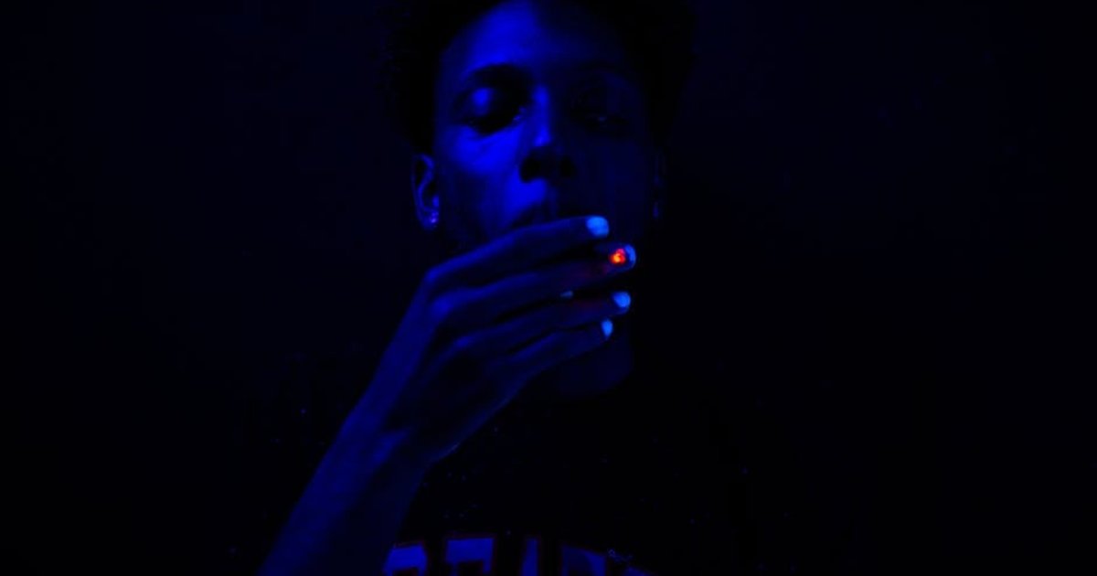Close-up of a man smoking under blue ultraviolet lighting, creating a dramatic effect.