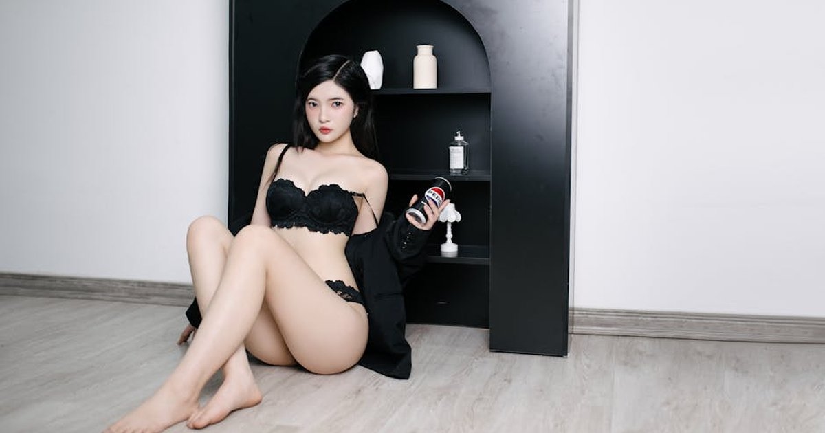 Woman in black lingerie sitting against a black shelf, creating a stylish indoor scene.