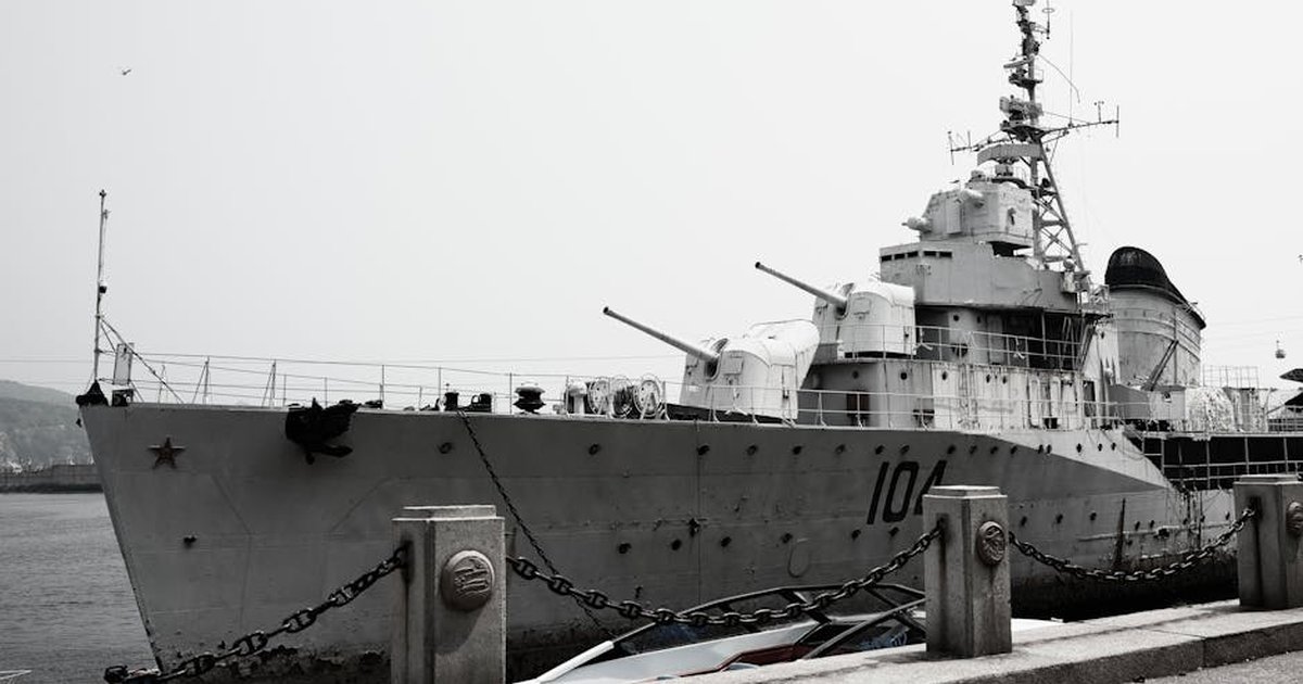 A large naval destroyer ship docked at a harbor under a gray sky.
