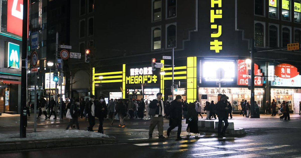 Bustling nighttime street scene in Sapporo, Hokkaido with neon lights and pedestrians.