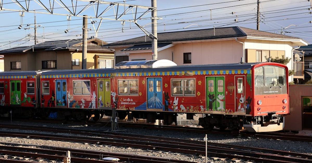Vibrant train with cartoon designs in Japanese neighborhood under clear skies.