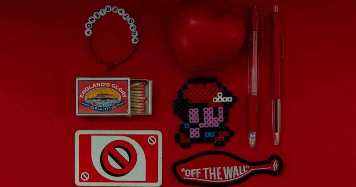 Creative flat lay featuring red objects including heart, pens, pixel art, and matchbox.