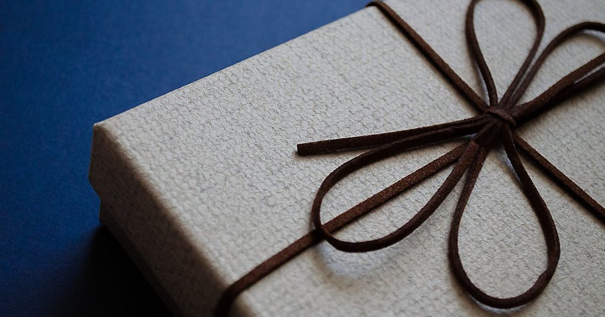 Close-up of an elegant gift box with a brown leather bow on a blue surface, perfect for special occasions.