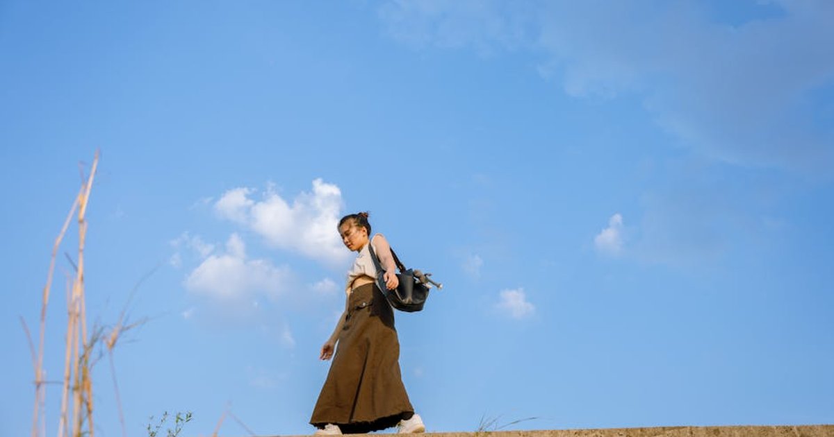 A woman walks casually with a backpack under a clear blue sky, exuding a sense of freedom and exploration.