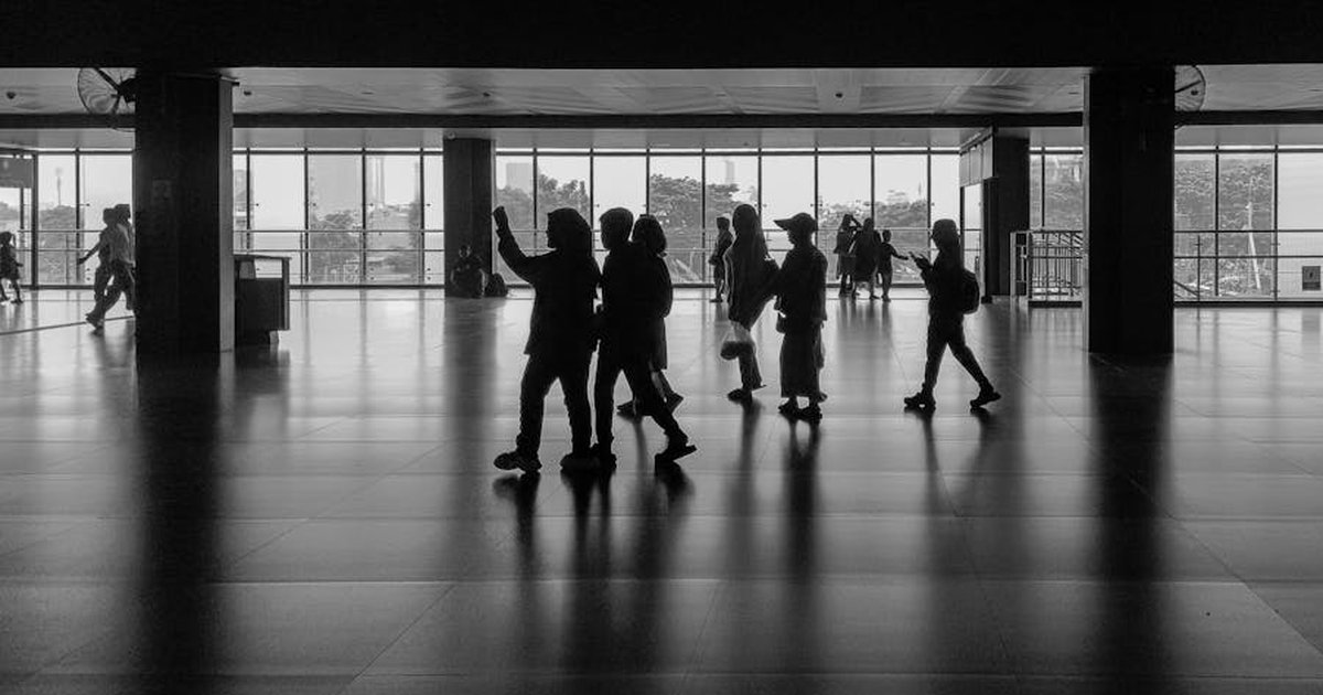 Silhouettes of people walking in an indoor Jakarta station, shot in black and white.