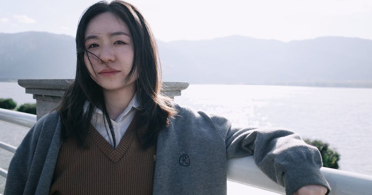 Young woman enjoys a sunny day by Dianchi Lake with mountains in the background, capturing a serene moment.