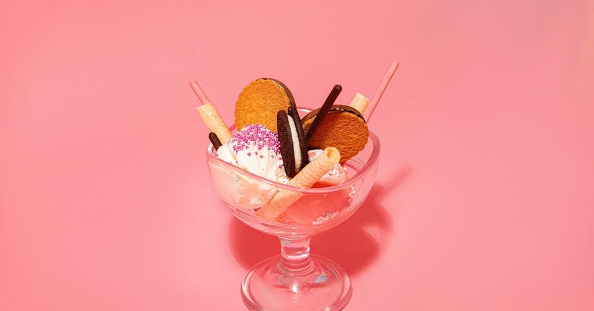 Glass of delicious gelato scoops with vanilla waffle rolls and crispy biscuits with smooth filling on pink background