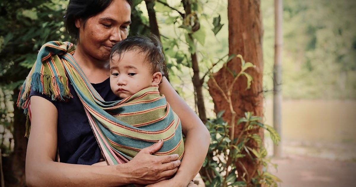 A mother lovingly cradles her child in a colorful sling amidst the natural beauty of Vietnam's Kon Tum.
