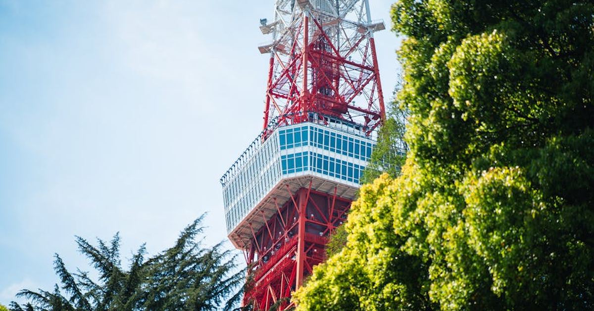 A striking view of Tokyo Tower rising above lush green trees under a bright blue sky.