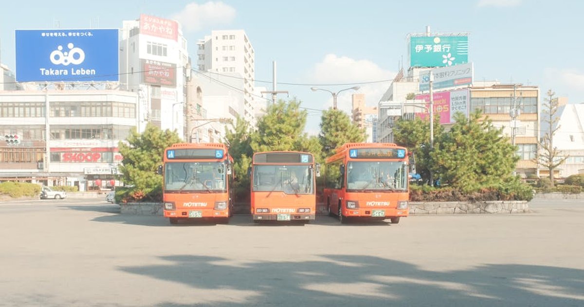 Orange buses parked in urban Japan street with cityscape background.