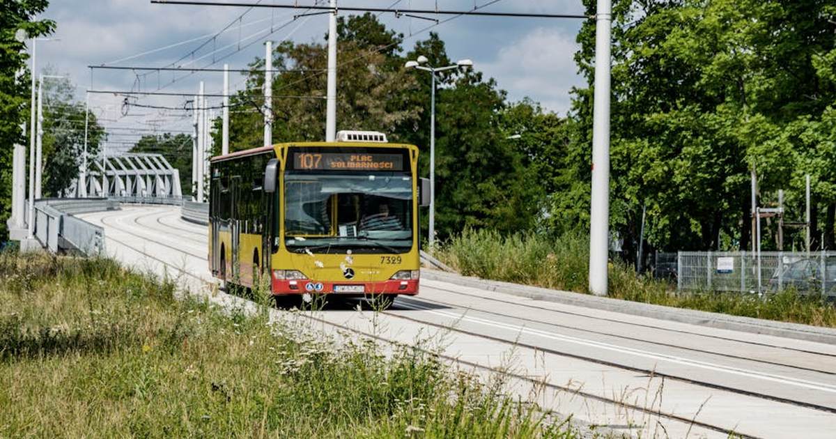 City bus crossing an overpass in Wrocław, Poland, amidst green surroundings.