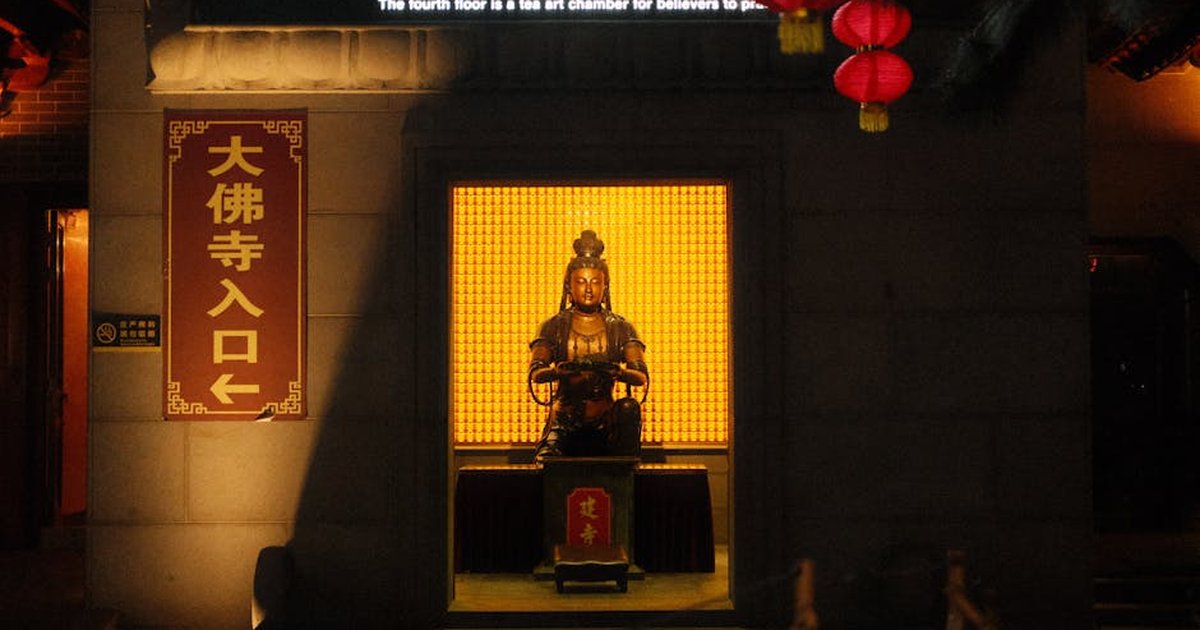 A Buddha statue illuminated at the entrance of a temple, surrounded by lanterns at night.