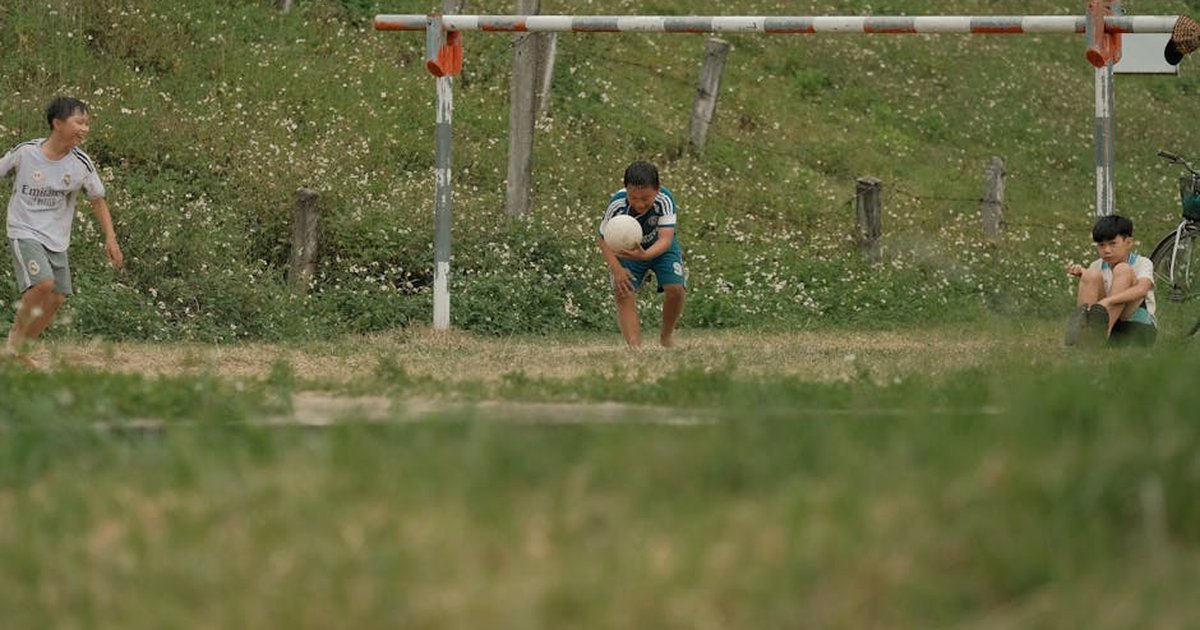 Three kids enjoying a casual soccer game in a grassy field, capturing summer fun.