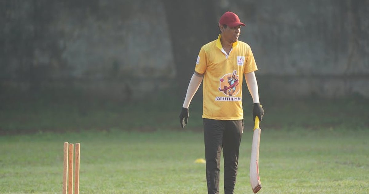 Cricketer in action on a sunny day, holding bat on green field.