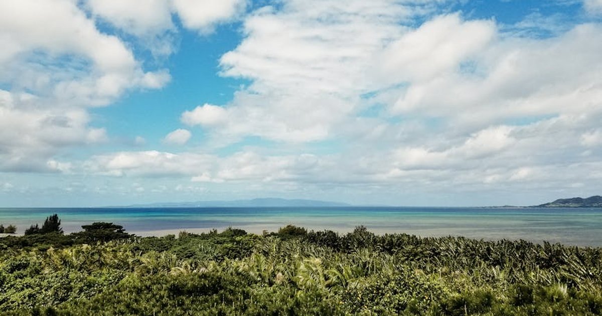 A tranquil coastal landscape with lush greenery, a blue sea, and a partly cloudy sky.