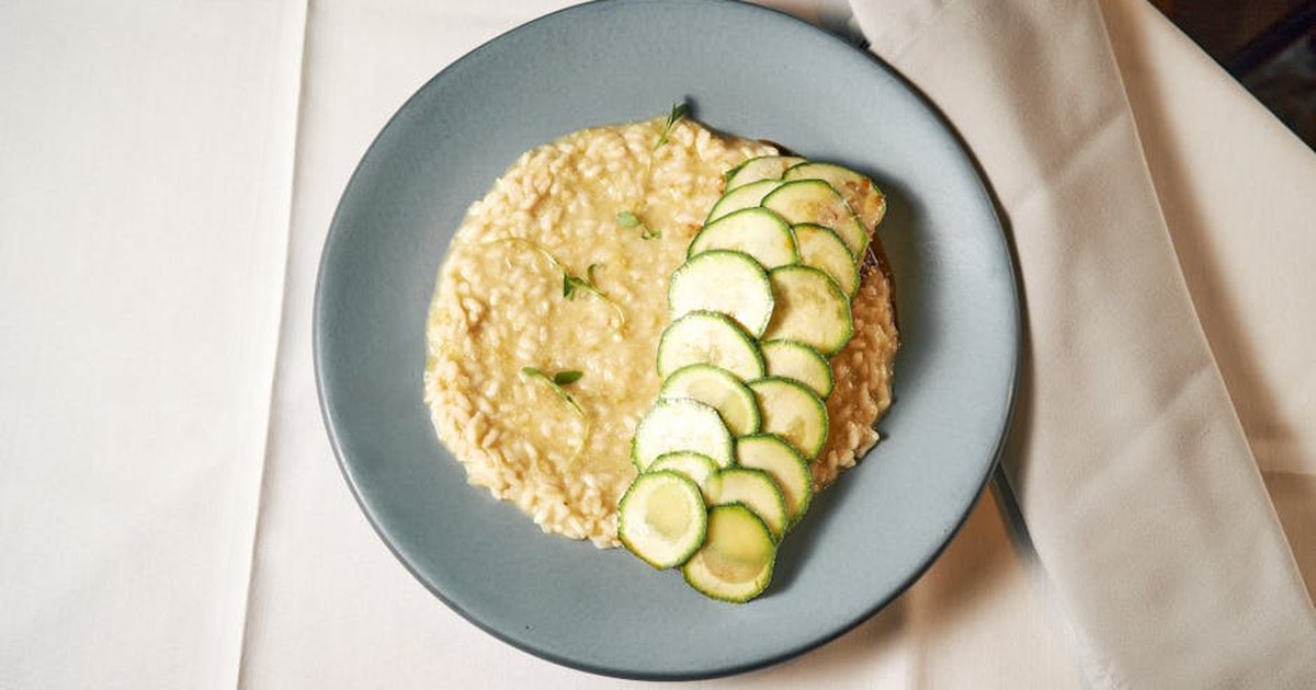 Creamy risotto served with fresh zucchini slices on a stylish table setting.
