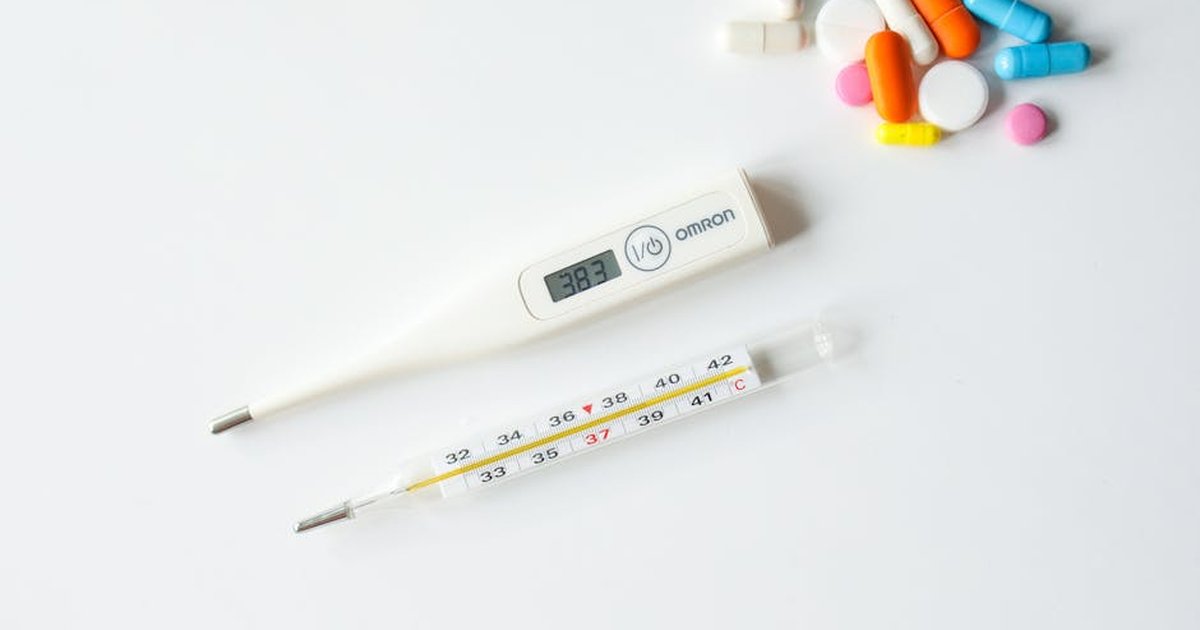 Digital and glass thermometers with colorful pills on white background.
