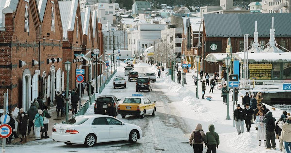 A vibrant winter street scene in Hakodate, Japan, with people and cars on a snowy day.
