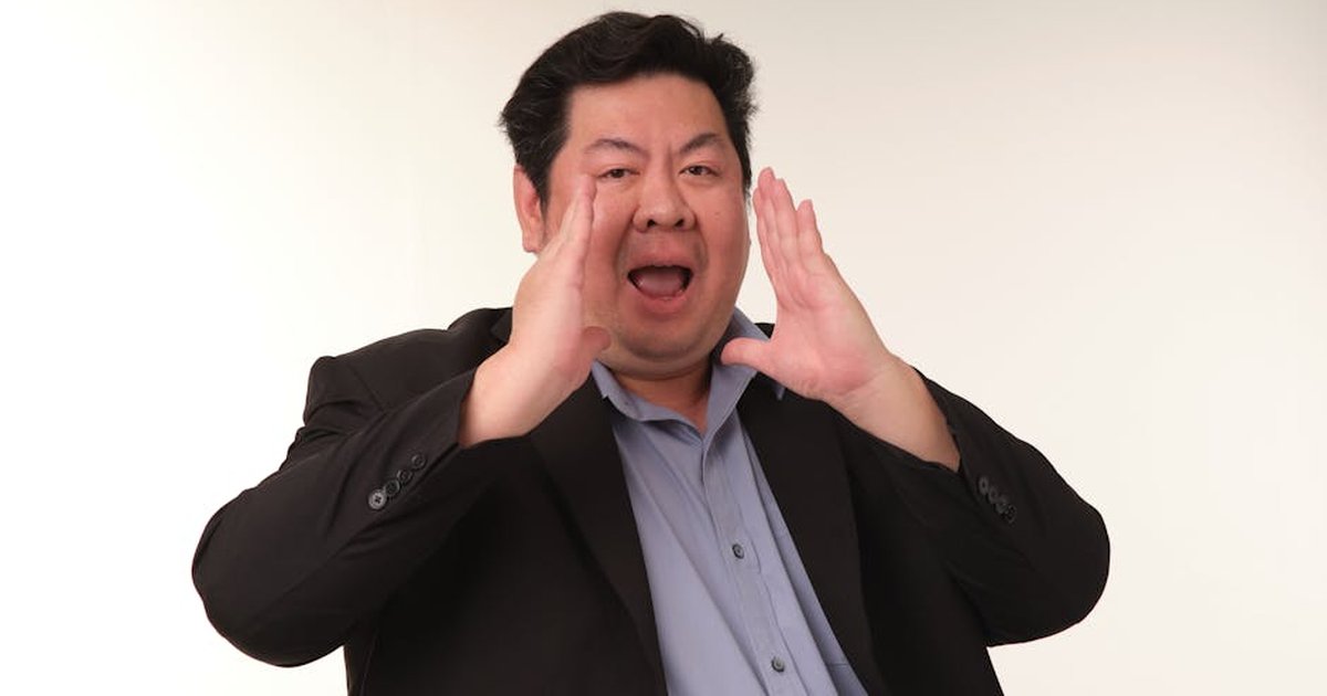Asian adult man shouting with hands around mouth in a studio setting.