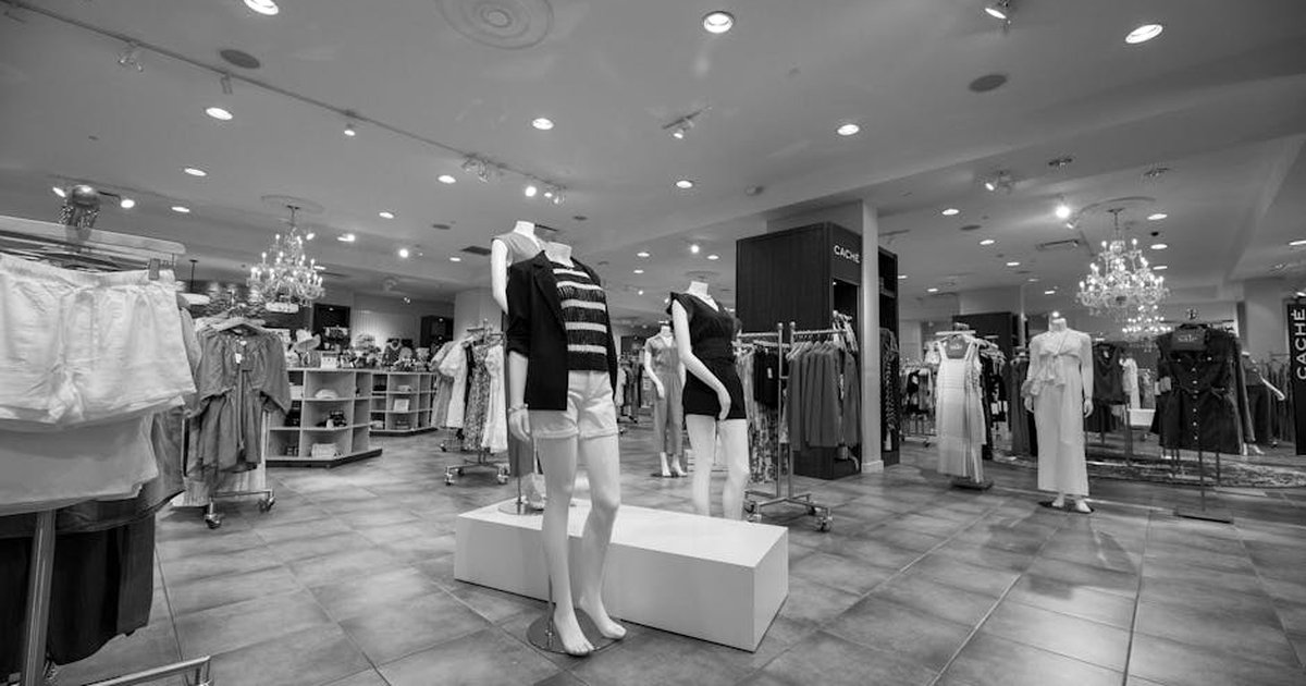 Black and white image of a fashion store interior featuring mannequins and clothing displays.