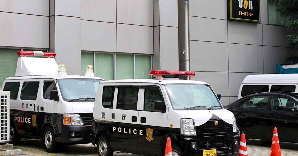 Police vans in Tokyo, Japan, parked outside a building with traffic cones.