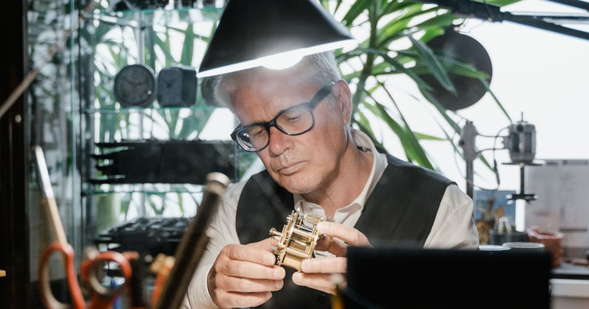 Experienced artisan focused on intricate clock mechanism repair in well-lit workshop.