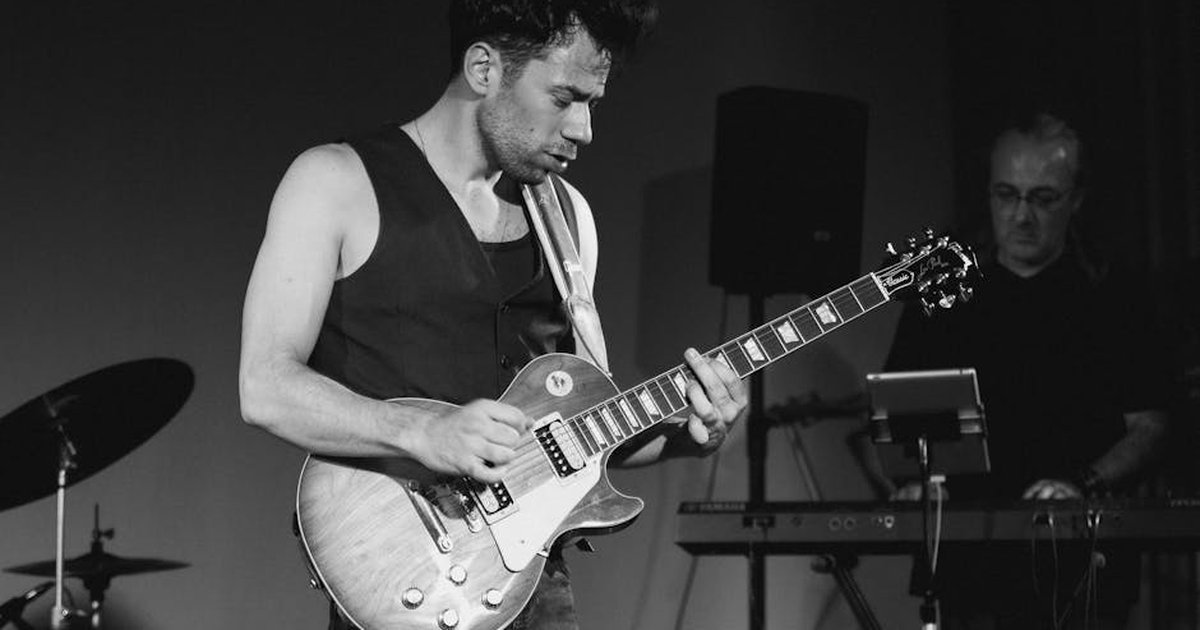 Black and white photo of a guitarist playing live on stage during a music performance.
