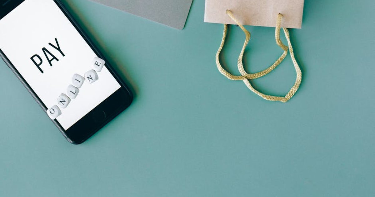 Illustration of online payment with smartphone, credit card, and shopping bag on mint background.