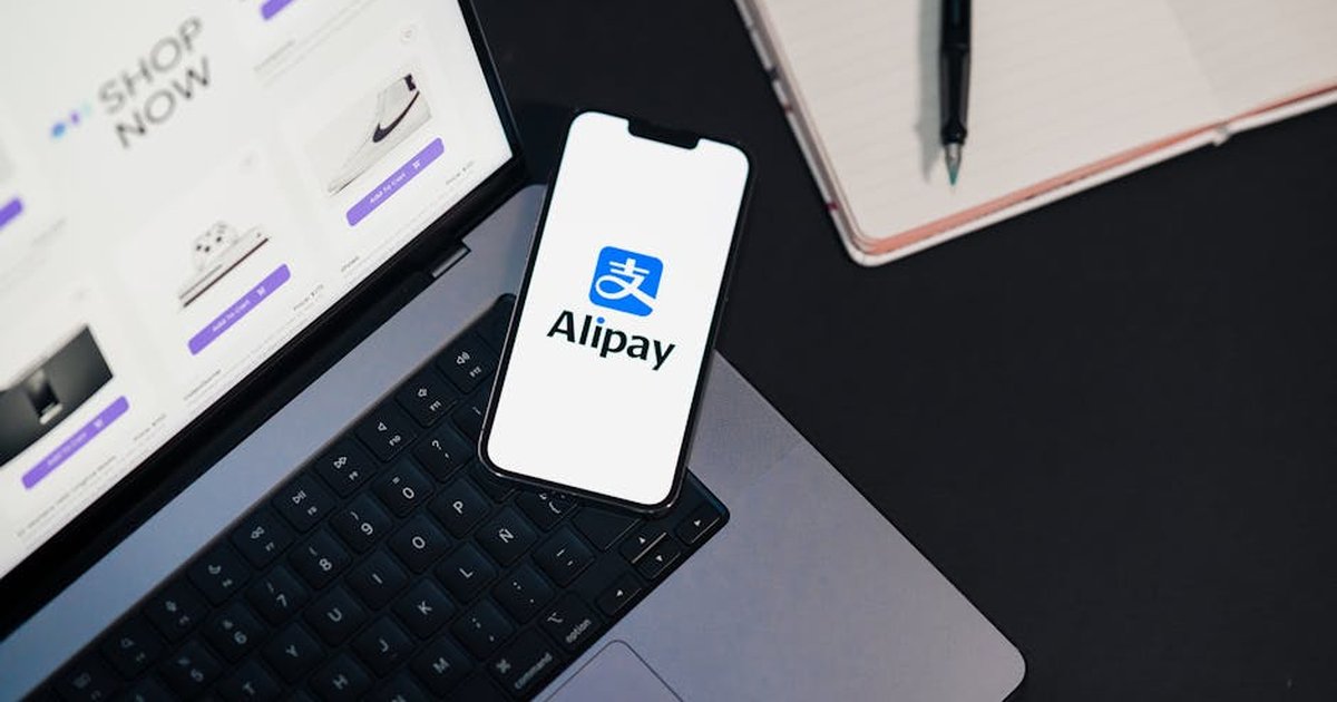 Smartphone displaying Alipay app on open laptop with online shopping site.