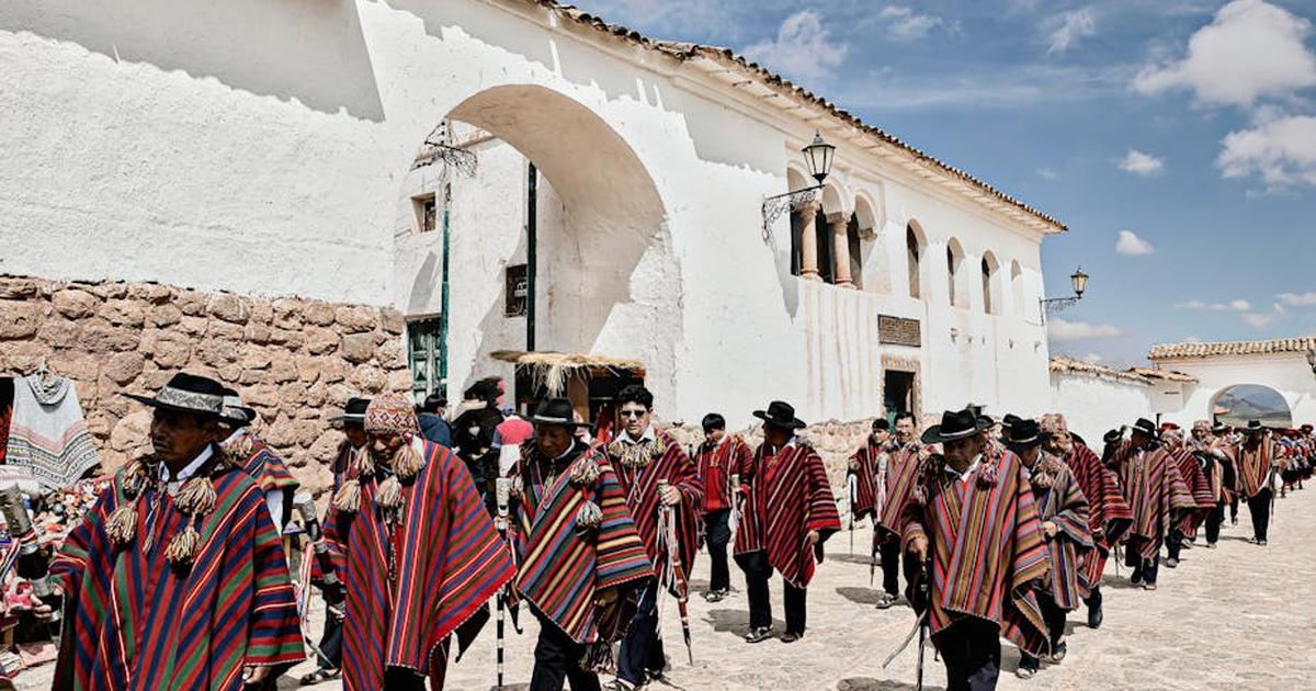 Group of people in colorful attire walking in Andean town square during a traditional festival.