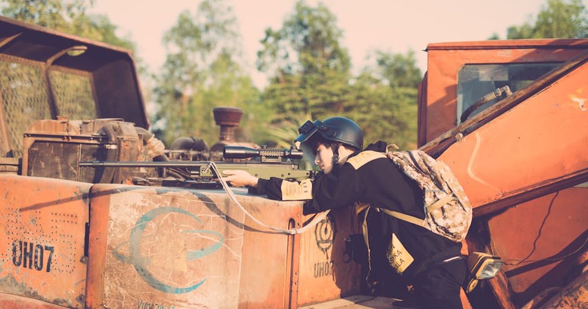 Person engaging in realistic outdoor play with a toy sniper rifle on industrial machinery.