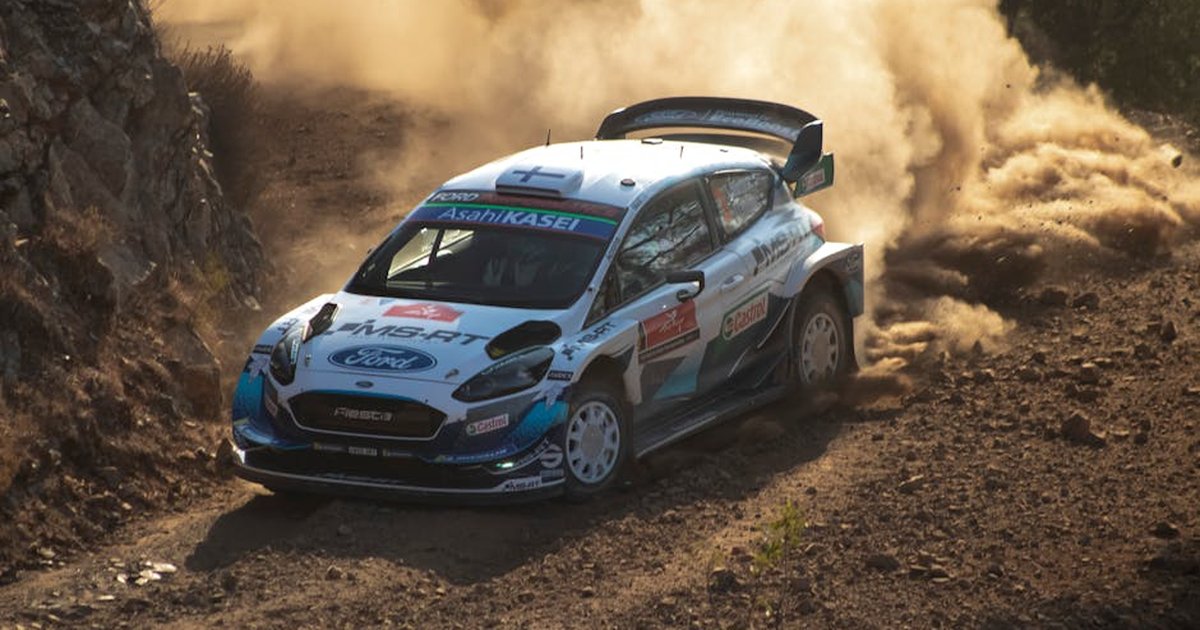 Rally car powers through dusty dirt road corner, showcasing speed and control in an outdoor off-road race.