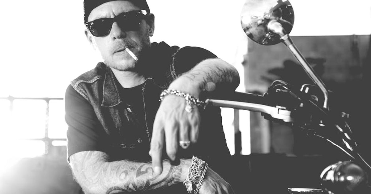 Black and white portrait of a man in sunglasses, smoking, sitting on a motorcycle.
