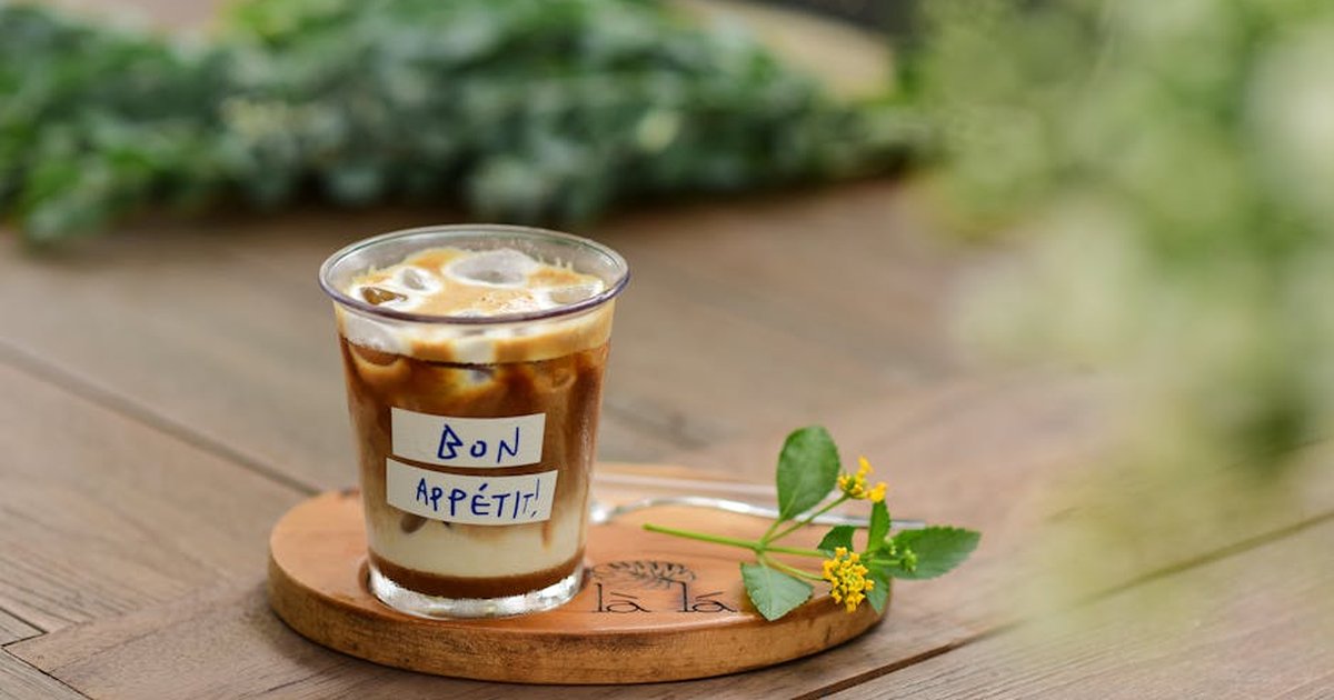 A cup of coffee with foam served on a wooden tray displaying the note 'Bon Appétit!'
