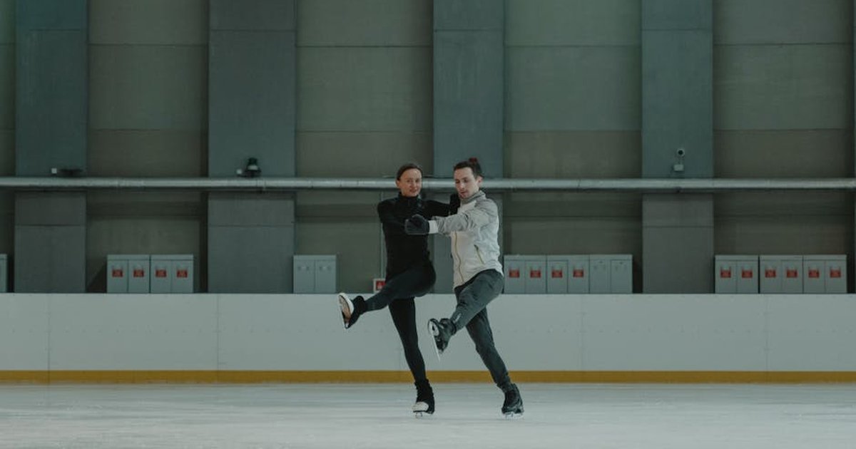 A couple gracefully practices figure skating moves on an indoor rink, showcasing balance and skill.