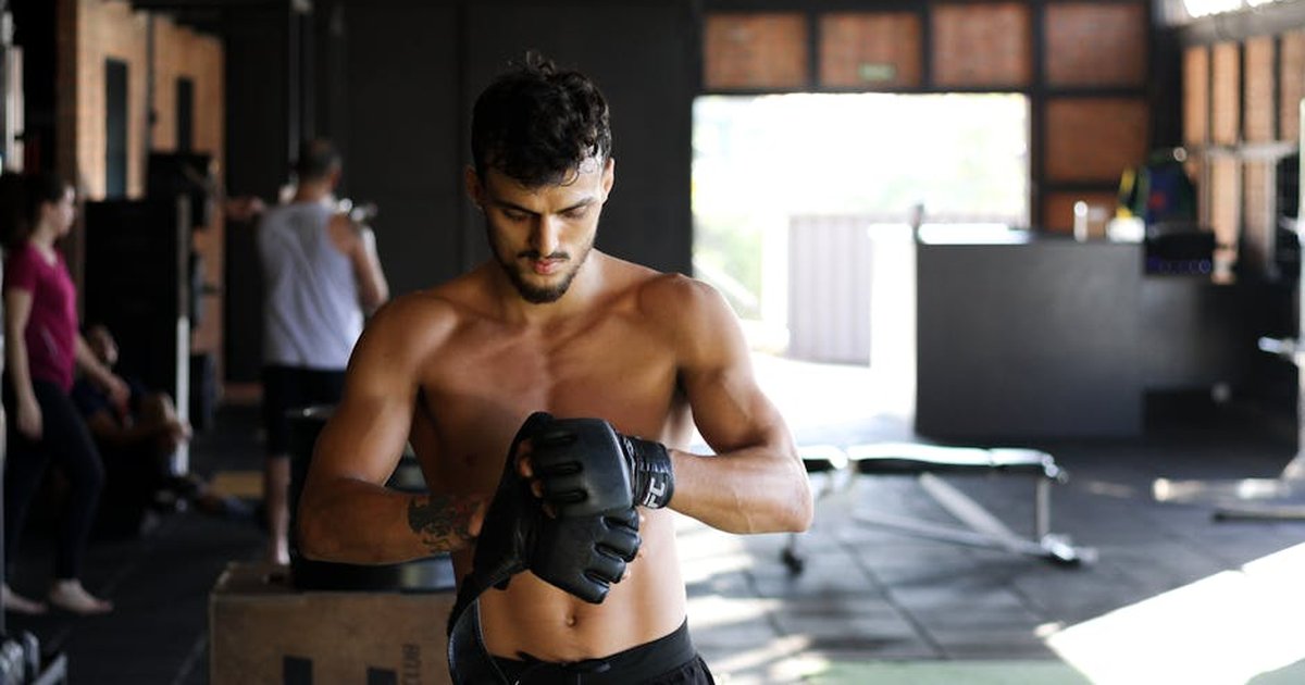 Shirtless man preparing for an intense workout session in a gym, wearing boxing gloves.