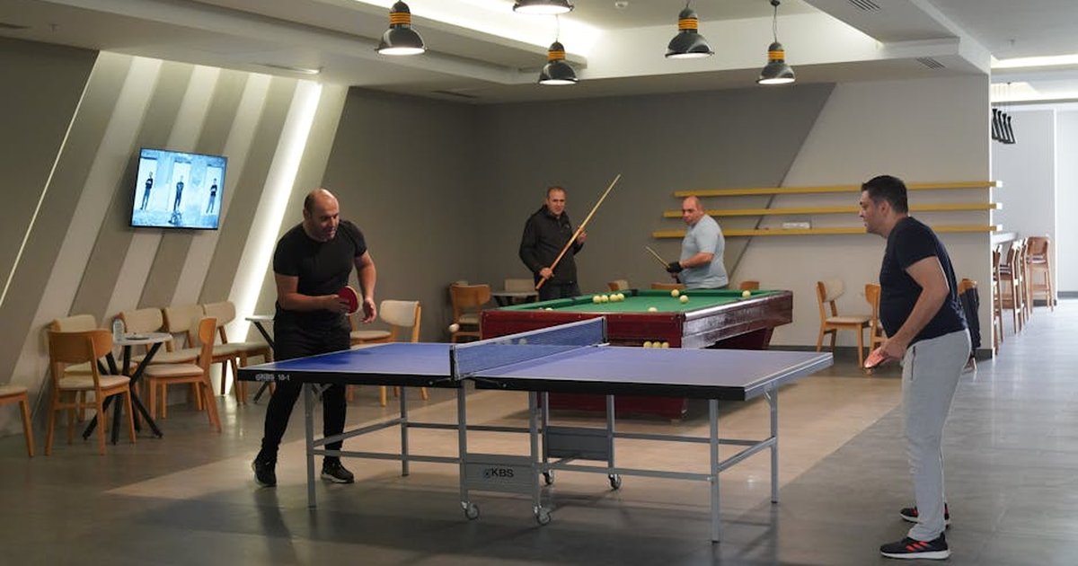 Group of men enjoying table tennis and billiards in an indoor recreational center.