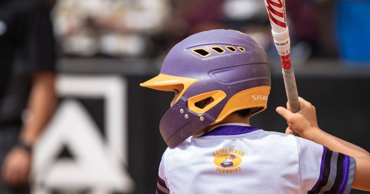 A child wearing a helmet and holding a bat is ready to play baseball in a park.