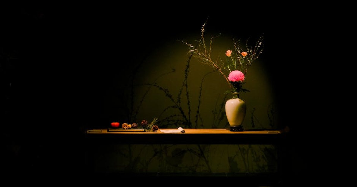 A vase with pink and orange flowers under spotlight on a wooden table with a dark background.