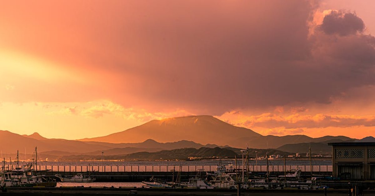 Tranquil harbor scene with boats and mountain backdrop during a vibrant sunset.