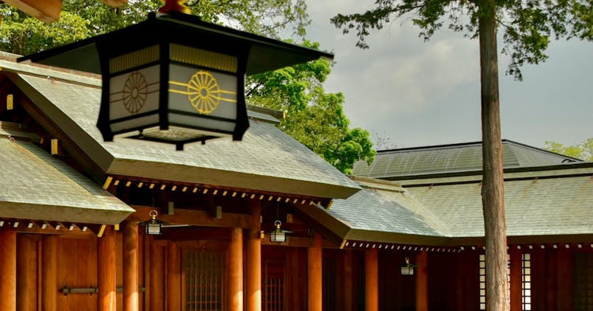 A peaceful view of a traditional Japanese Shinto shrine features a hanging lantern in the foreground.