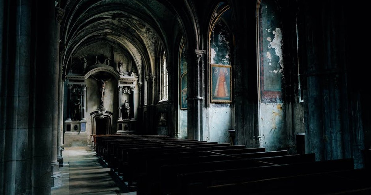 Dimly lit Gothic church interior showcasing arched columns and religious artworks.