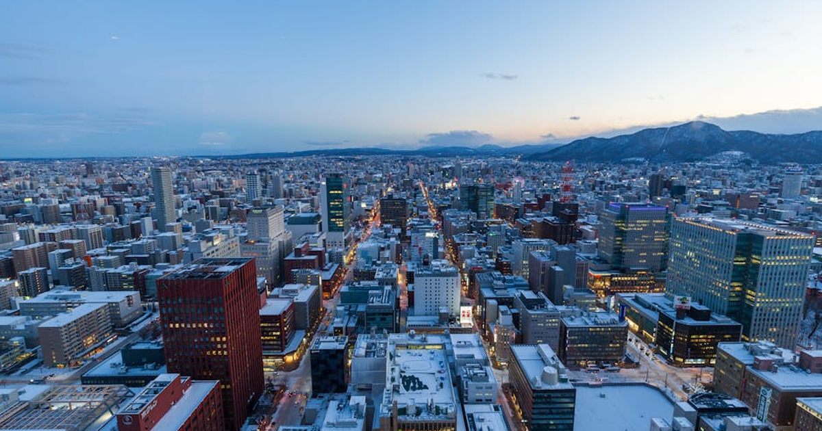 Captivating aerial view of Sapporo, Japan in winter at dusk with snow-covered buildings and distant mountains.