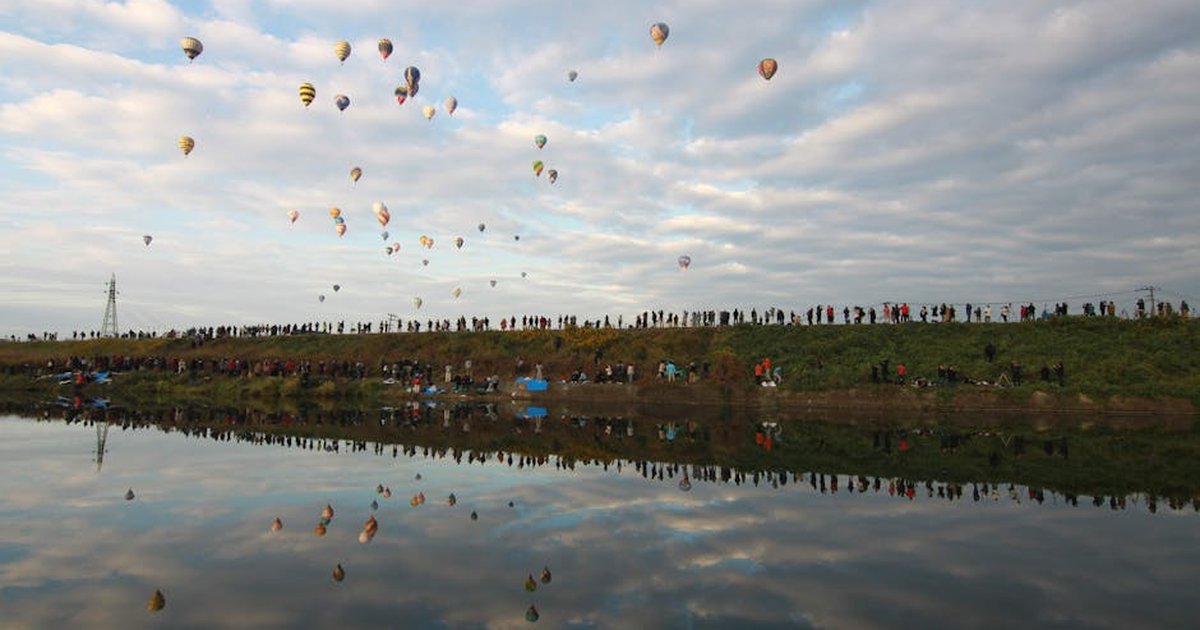 Vibrant hot air balloons soar over a calm lake with reflections in Saga, Japan.