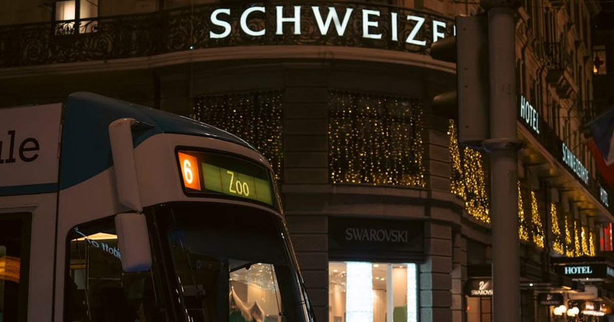 Urban evening scene with a tram passing by illuminated shops in a bustling city center.