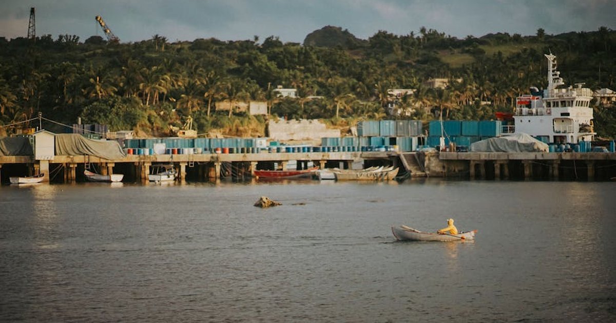 A serene view of Basco harbor in the Philippines with a rowboat and lush greenery.