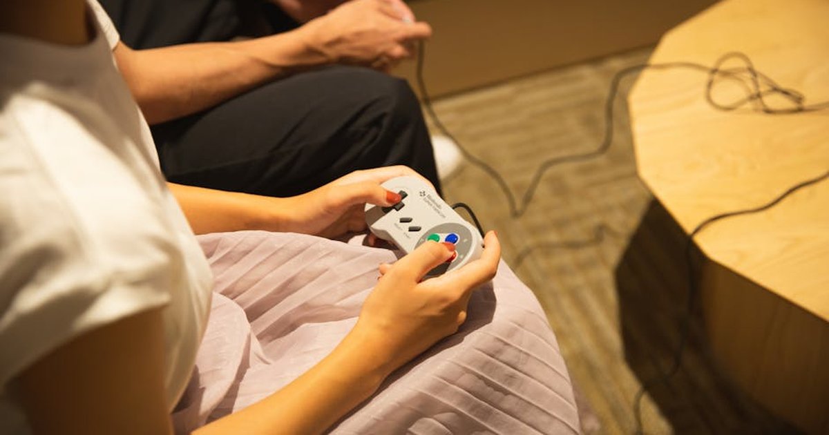 From above of crop anonymous man and woman in casual clothes playing video game with joysticks while spending weekend together at home