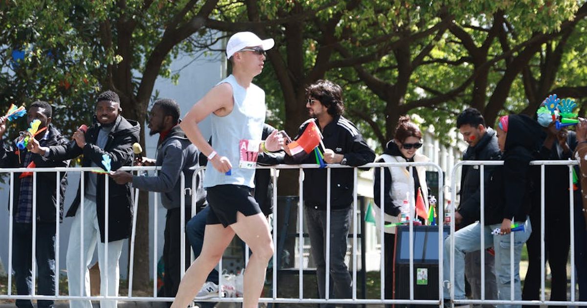 A marathon runner passes a cheering crowd outdoors on a sunny day.